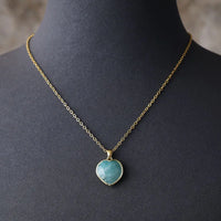 A gold-tone chain necklace with a heart-shaped Amazonite pendant displayed on a mannequin. ALLORA JADE