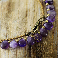 Close-up of a purple Amethyst and seed bead necklace laid out on a wooden surface. ALLORA JADE