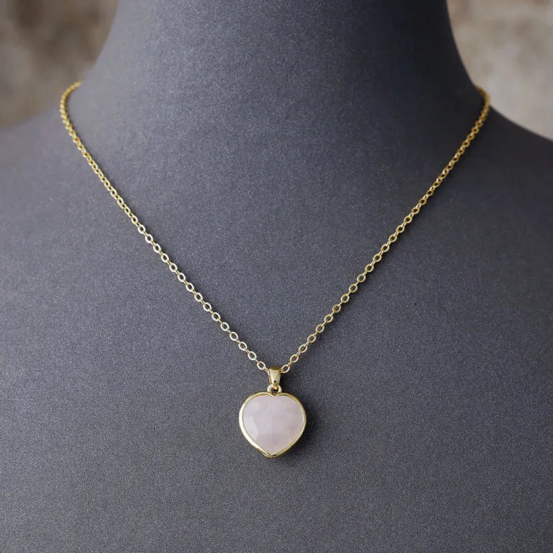 A gold-tone chain necklace with a heart-shaped rose quartz pendant, displayed on a mannequin. ALLORA JADE