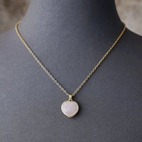 A gold-tone chain necklace with a heart-shaped rose quartz pendant, displayed on a mannequin. ALLORA JADE
