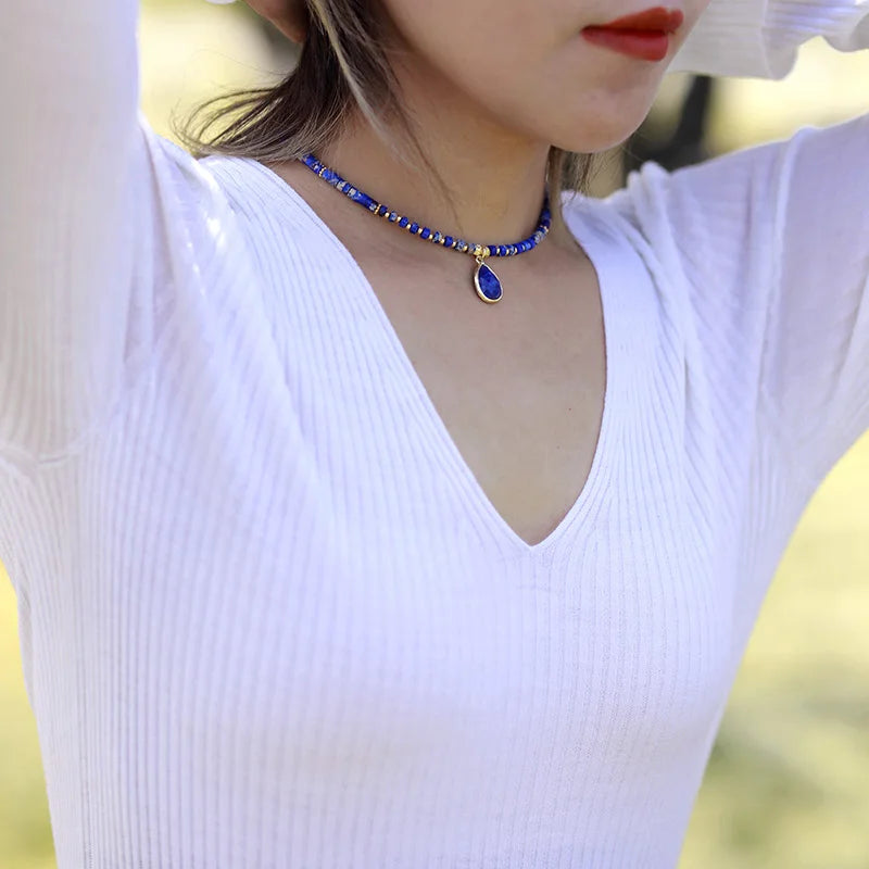 A person wearing a white V-neck top and showcasing a blue choker necklace with crystal charms and beads. ALLORA JADE