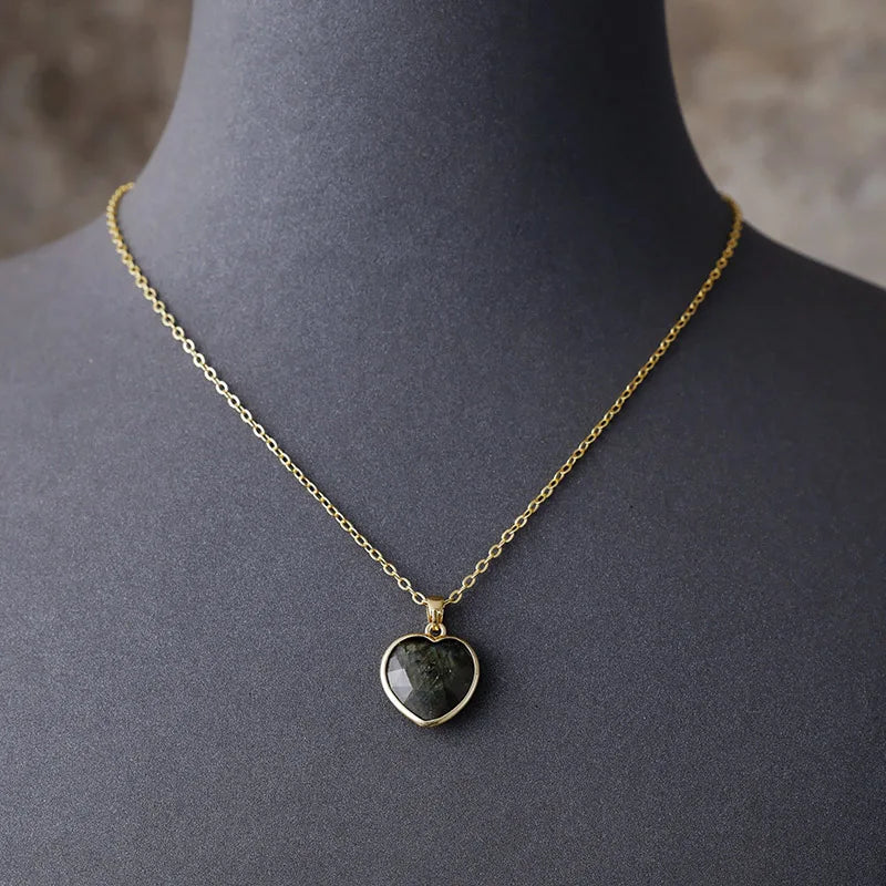 A gold-tone necklace with a heart-shaped labradorite pendant displayed on a mannequin. ALLORA JADE