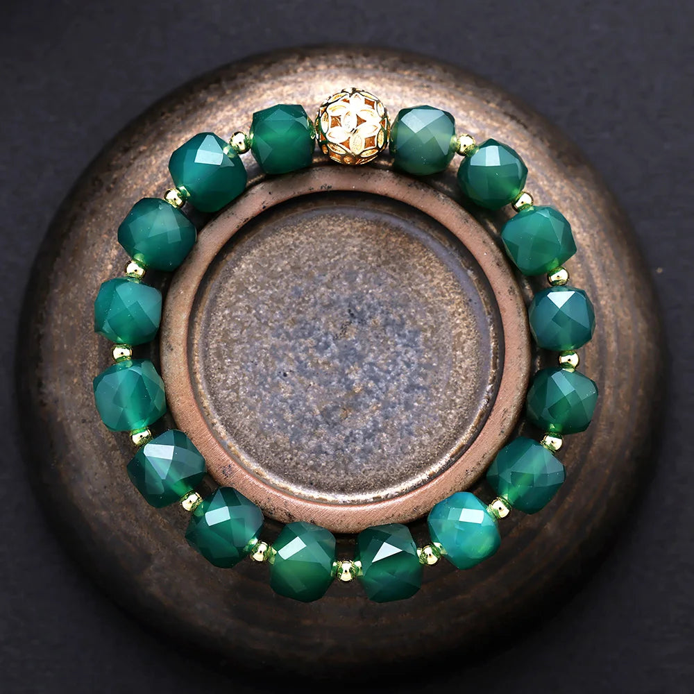 Green beaded bracelet with a gold clasp on a dark surface. ALLORA JADE