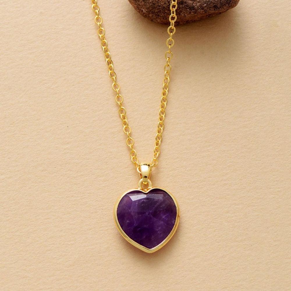 A heart-shaped Amethyst pendant necklace on a gold chain, displayed against a beige background.