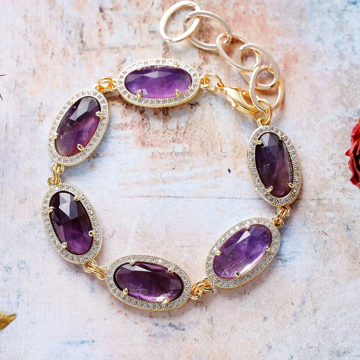 Gold bracelet with purple gemstones on a textured surface