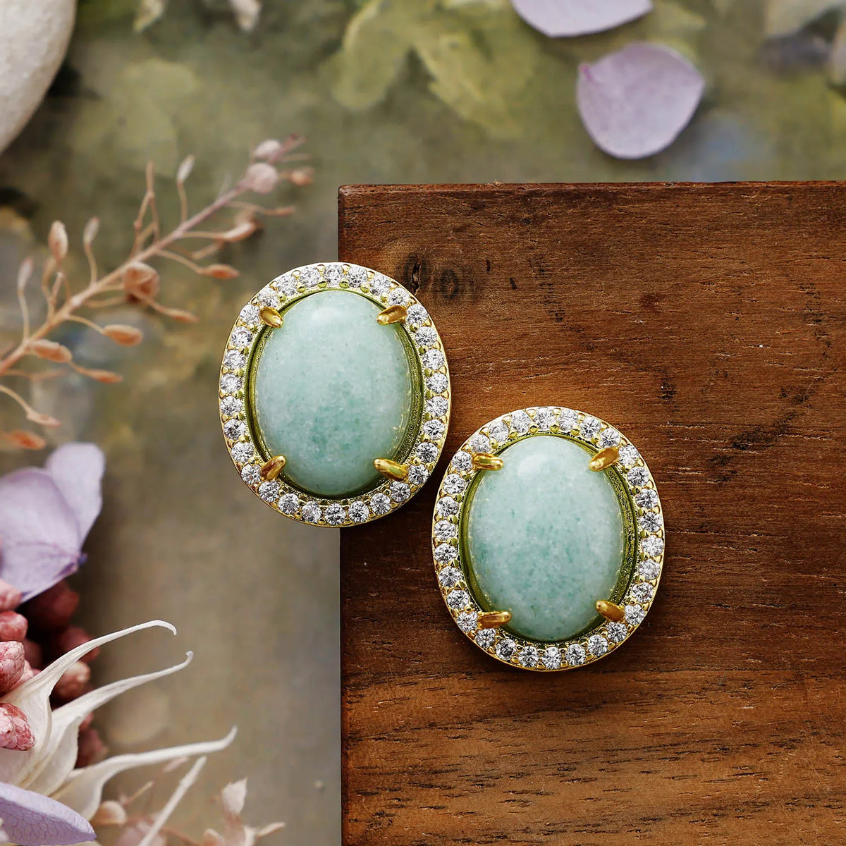 Amazonite Pavé Oval Stud Earrings featuring polished blue-green gemstones framed by sparkling rhinestones in gold-coloured settings, displayed on rustic wood.