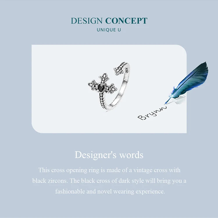 Adjustable silver cross ring with black zircon on a card with a feather and pen, against a light blue background.