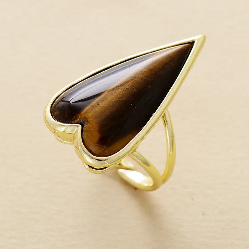 Gold ring with a large brown Tiger's Eye heart shaped gemstone on a beige background