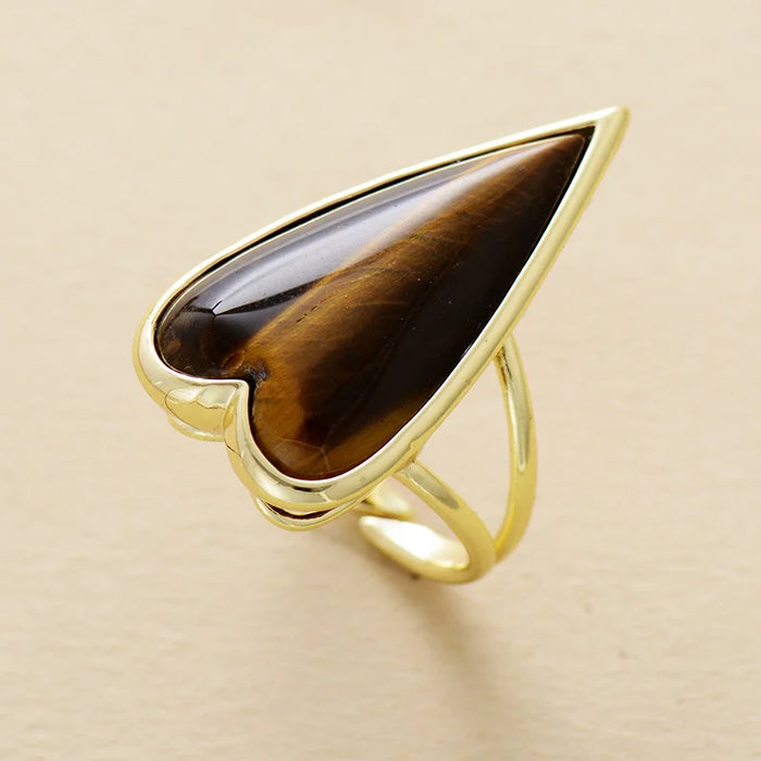 Gold ring with a large brown Tiger's Eye heart shaped gemstone on a beige background