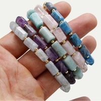 Close-up of a hand holding five beaded bracelets with a white background