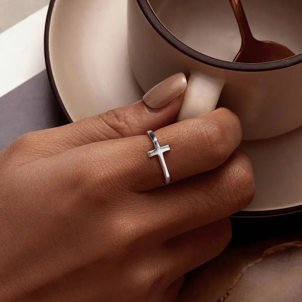 Hand wearing a silver cross ring with a cup in the background