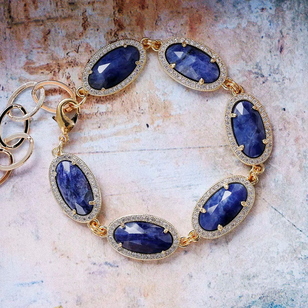 Gold bracelet with blue gemstones on a textured surface