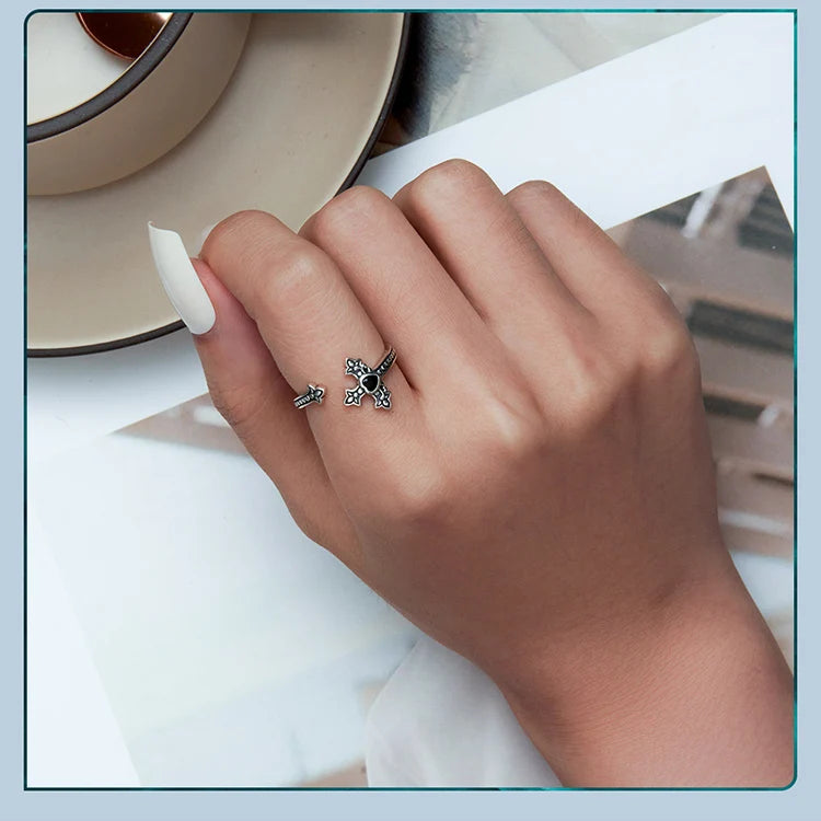 Hand wearing cross design open ring with black CZ on a light background