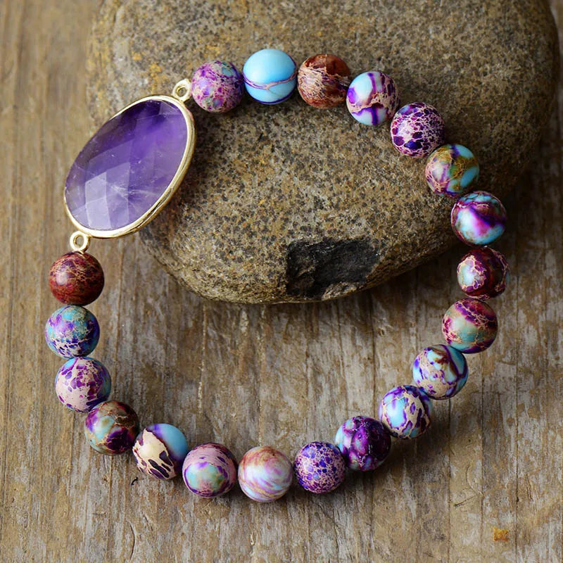 Multicolored beaded bracelet with a large purple stone on a stone surface