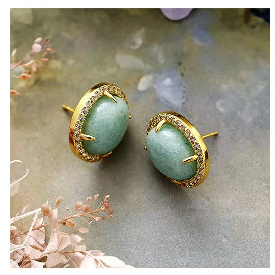 Amazonite Pavé Oval Stud Earrings featuring polished blue-green gemstones framed by sparkling rhinestones in gold-coloured settings, displayed on floral background.