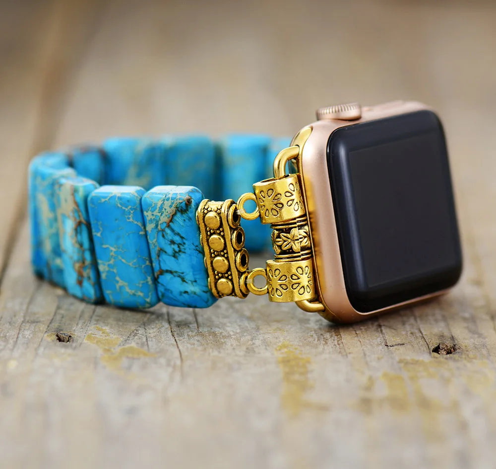 Smartwatch with a blue beaded bracelet on a wooden surface. Blue Jasper Stretchy Apple Watch Band | ALLORA JADE