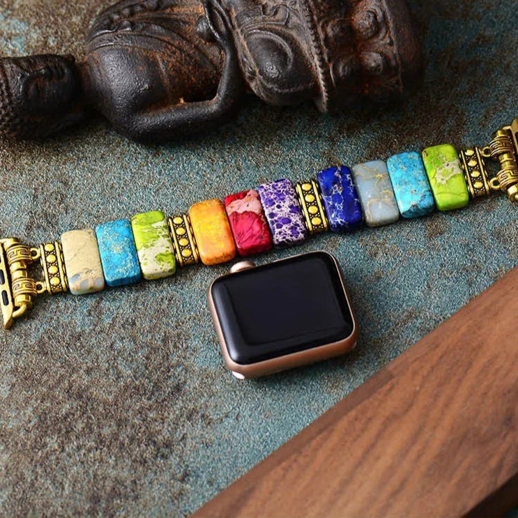 Colorful stone bracelet with a watch on a textured surface. 7 Chakras Jasper Stretchy Apple Watch Band | ALLORA JADE