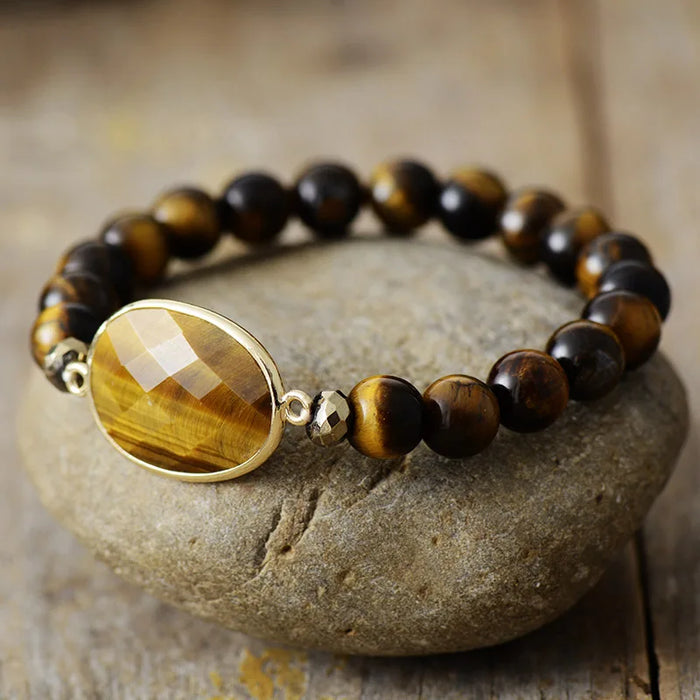 A stretchy bracelet with 8mm round Tiger's Eye beads and a faceted Tiger's Eye charm, displayed on a stone surface.