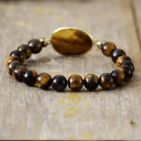 A stretchy bracelet with 8mm round Tiger's Eye beads and a faceted Tiger's Eye charm, displayed on a wooden surface.