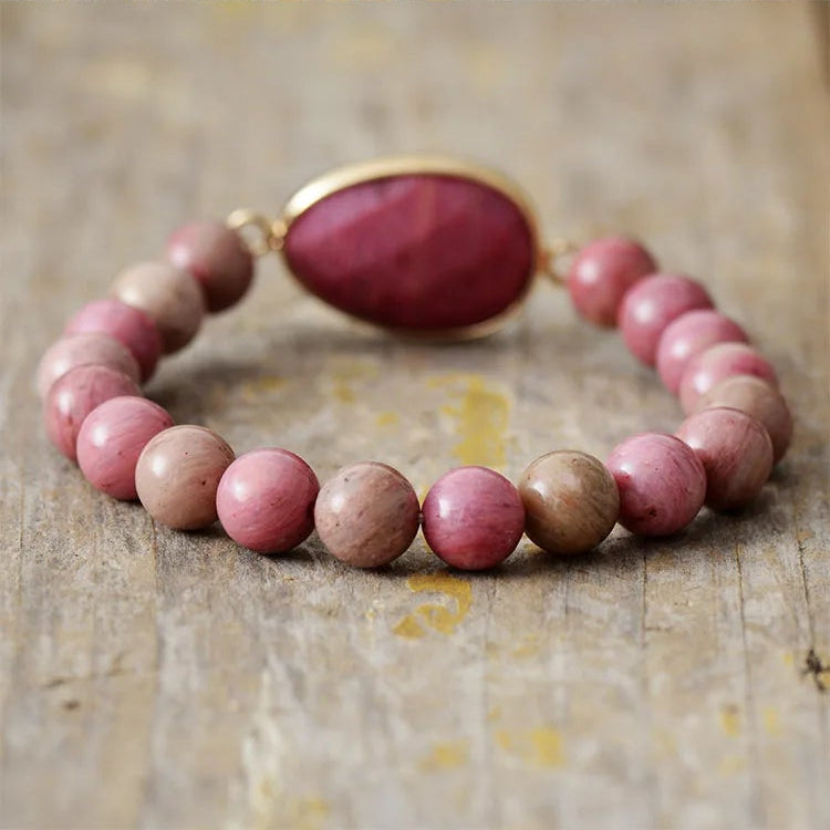 Beaded bracelet with pink and brown beads and a gold clasp on a wooden surface