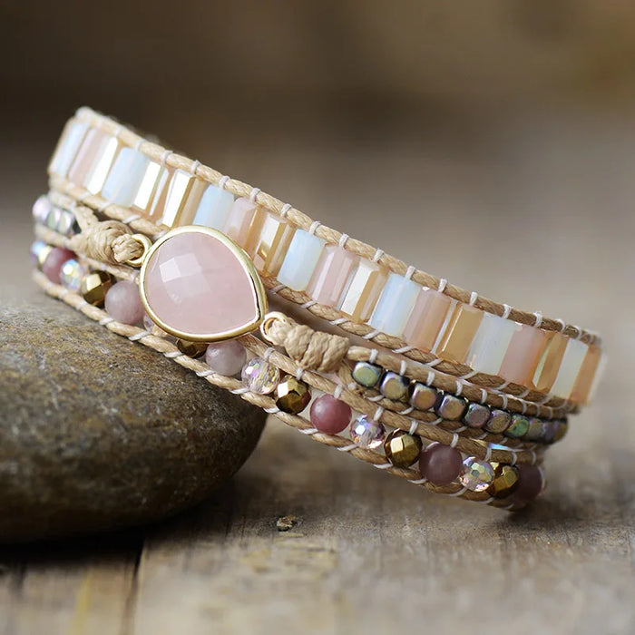Beaded bracelet with Rose Quartz gemstone charm, displayed on a stone surface