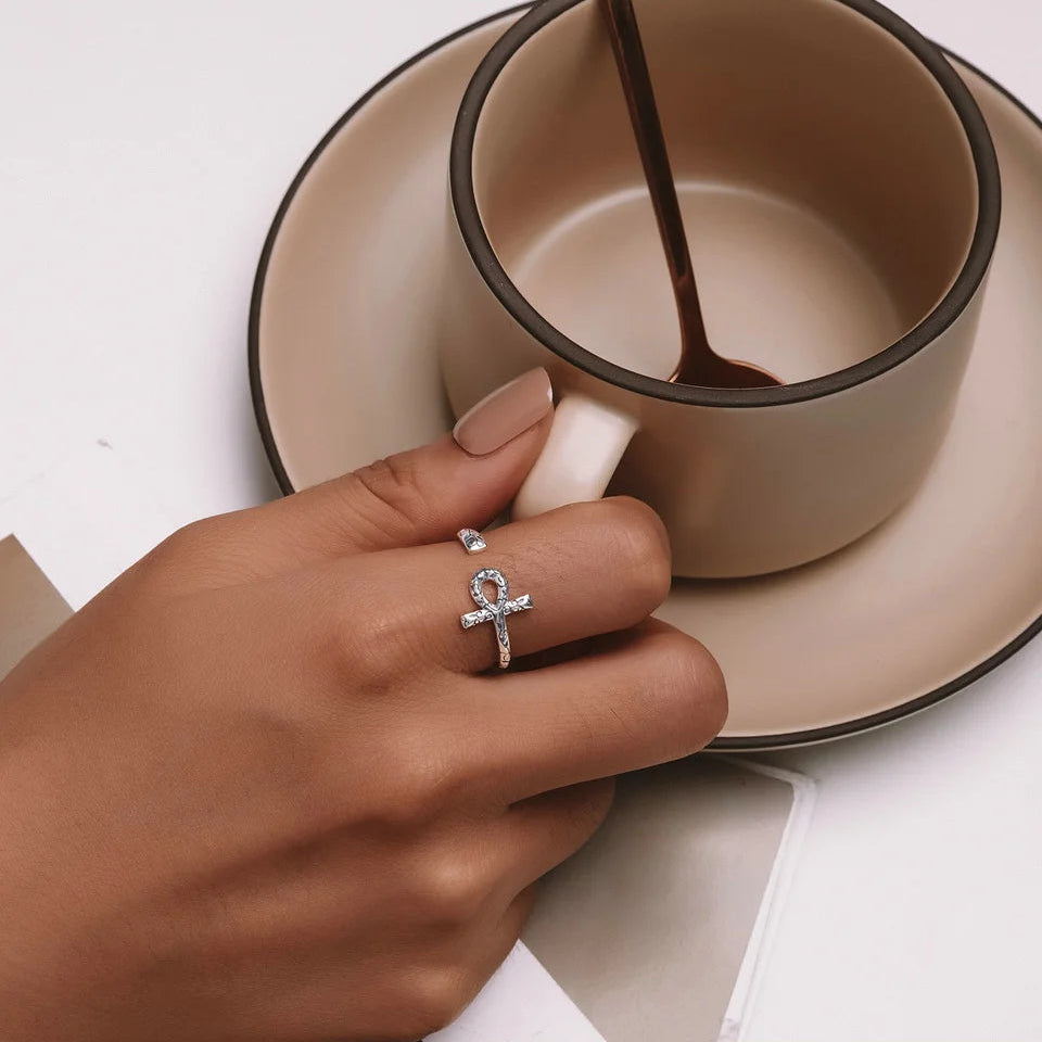Hand wearing a silver ring with an ankh design, holding a ceramic cup.