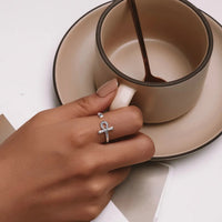 Hand wearing a silver ring with an ankh design, holding a ceramic cup.