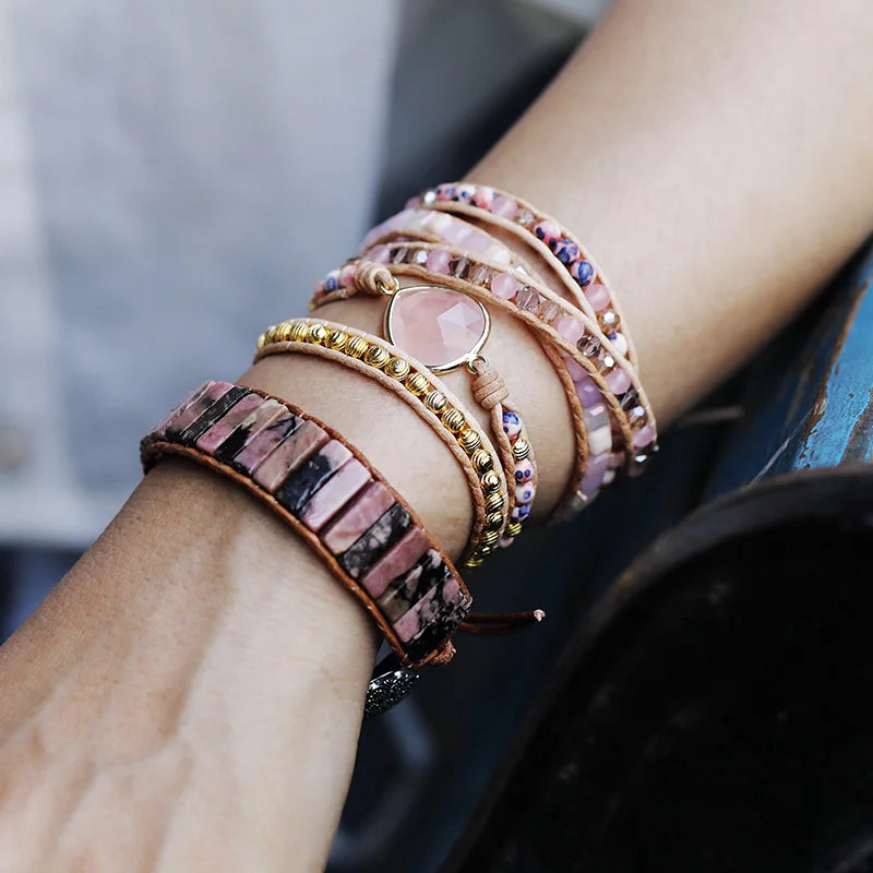 Close-up of a wrist wearing multiple colorful and pink beaded bracelets with a blurred background