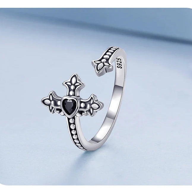 Silver ring with heart and cross design on a light blue background