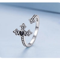 Silver ring with heart and cross design on a light blue background