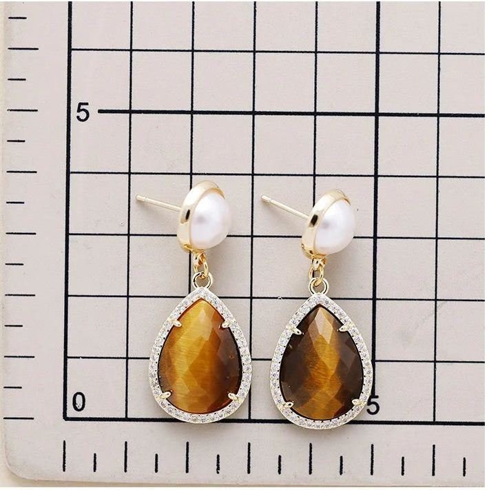 Tiger's Eye Pavé Teardrop Dangle Earrings featuring brown gemstone drops framed by sparkling rhinestones, with imitation pearl studs in gold-coloured settings on a scale background to show sizing.
