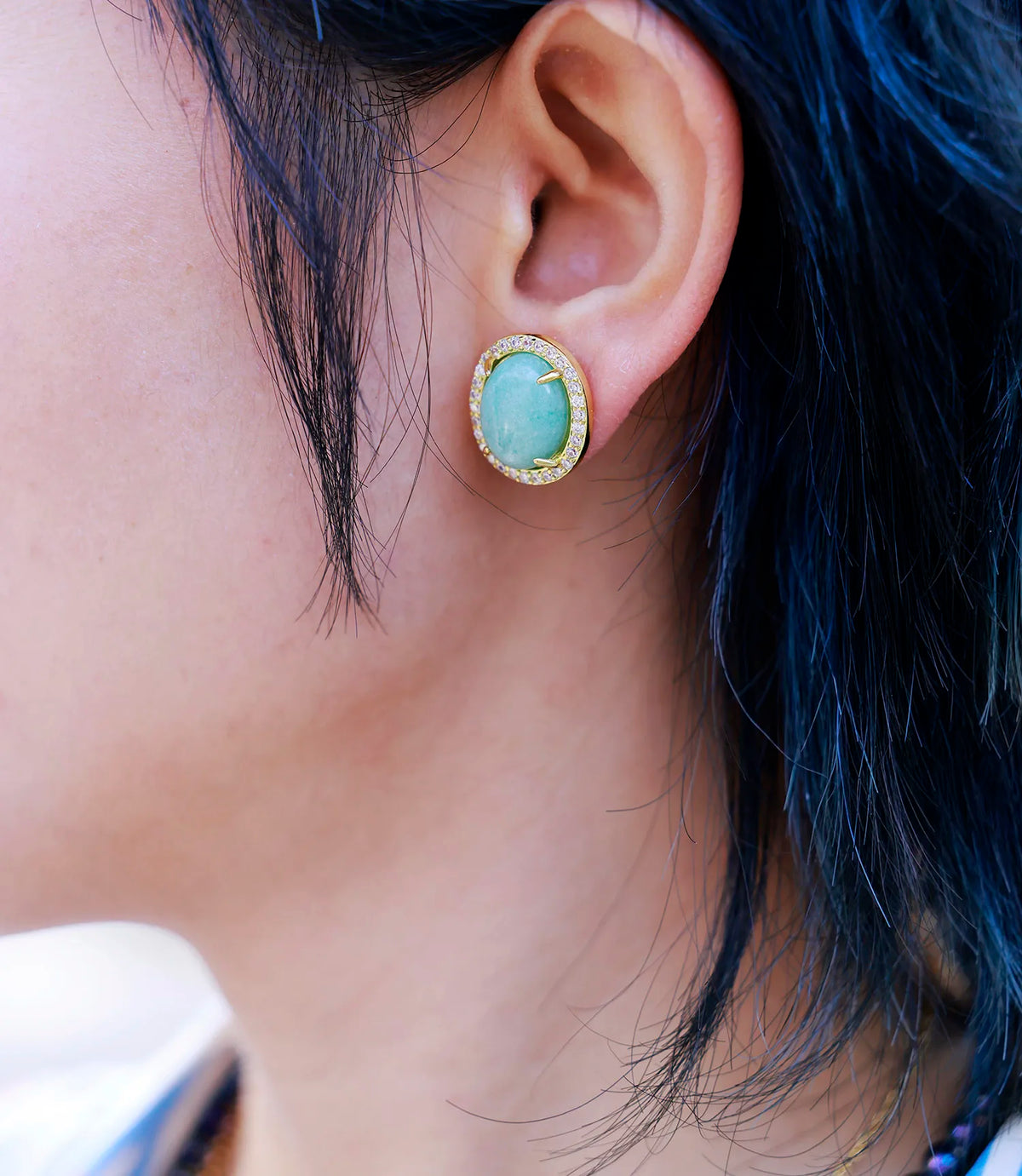 Close-up of a model wearing Amazonite Pavé Oval Stud Earrings, featuring soft blue-green gemstones surrounded by sparkling rhinestones in gold-coloured settings.