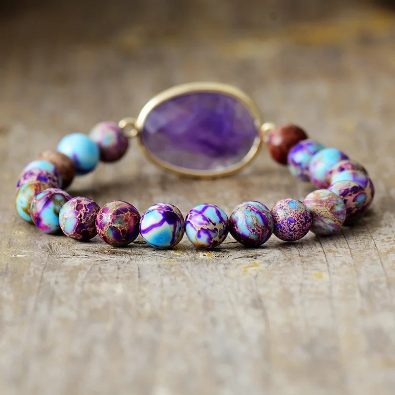 A stretchy bracelet with 8mm round Jasper beads and a faceted Amethyst charm, displayed on a wooden surface.