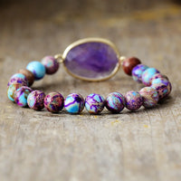 A stretchy bracelet with 8mm round Jasper beads and a faceted Amethyst charm, displayed on a wooden surface.