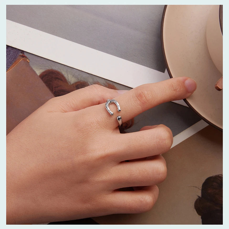 Hand wearing a silver ring with a horseshoe design on a neutral background
