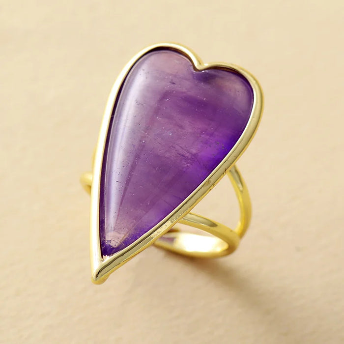 Gold ring with a heart-shaped purple Amethyst stone on a beige background