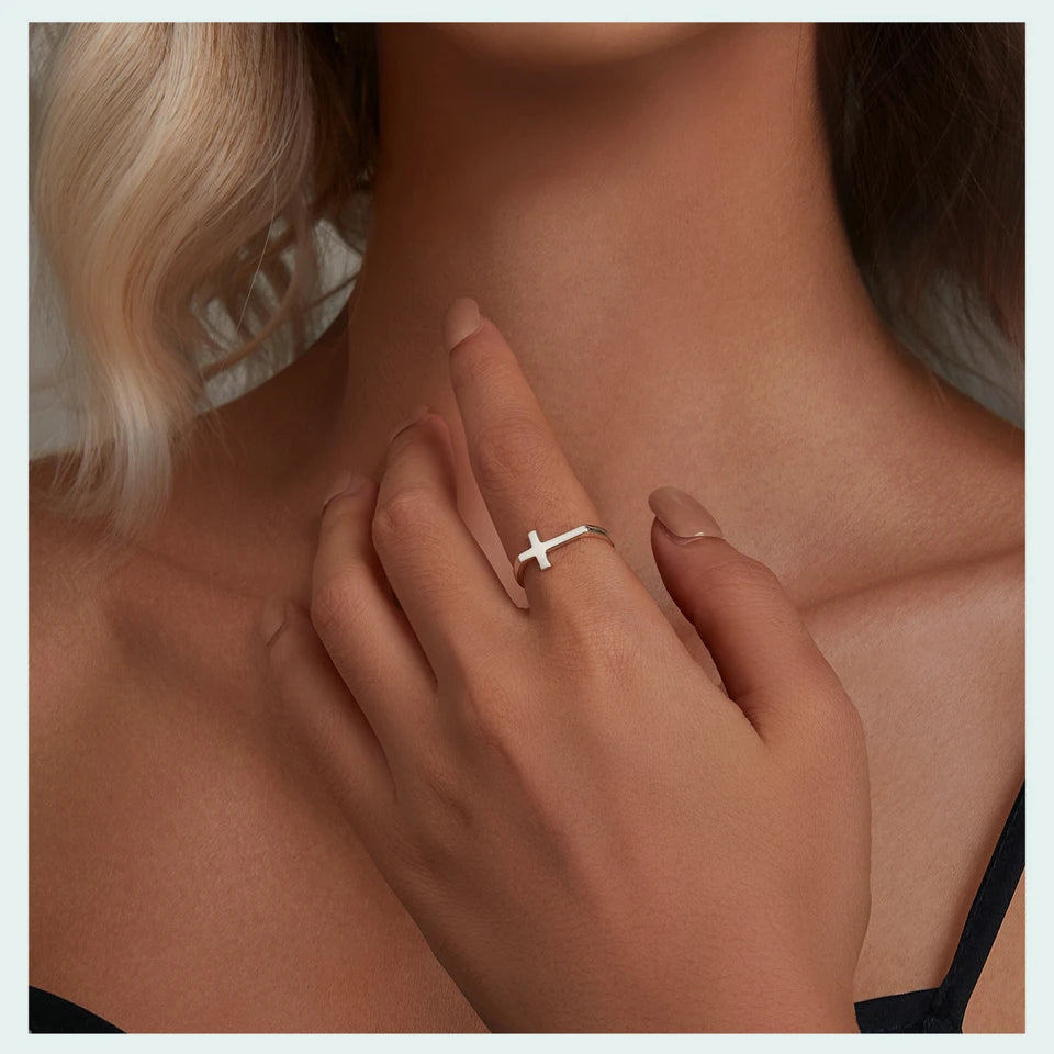 Close-up of a hand wearing a silver ring with a cross design, held against a neutral background.
