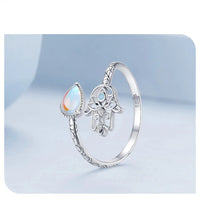 Silver ring with Hamsa hand design and tear-drop shaped CZ on a light blue background