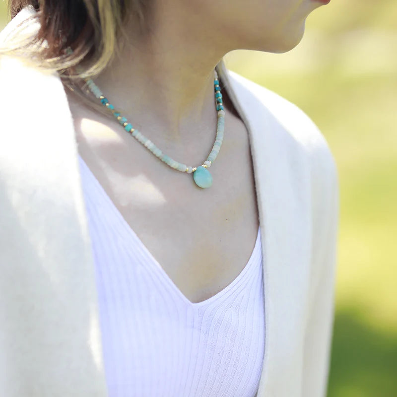 Person wearing a turquoise beaded necklace with a blurred natural background