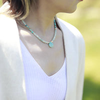 Person wearing a turquoise beaded necklace with a blurred natural background