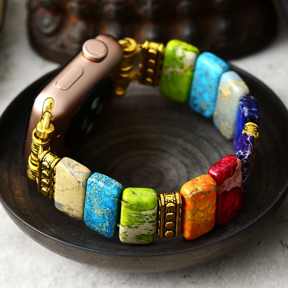 Colourful beaded bracelet with gold accents on a dark surface. 7 Chakras Jasper Stretchy Apple Watch Band | ALLORA JADE