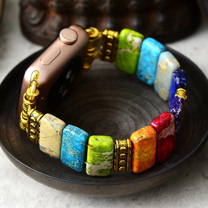 Colourful beaded bracelet with gold accents on a dark surface. 7 Chakras Jasper Stretchy Apple Watch Band | ALLORA JADE
