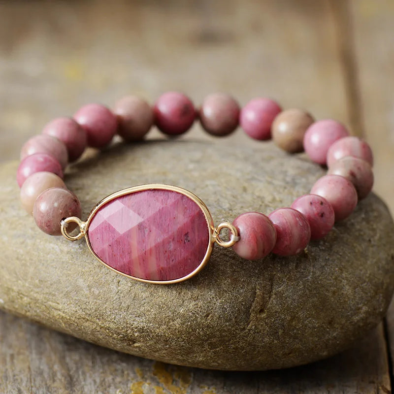 Pink beaded bracelet with a gold accent stone on a stone surface