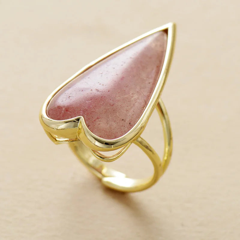 Gold ring with a heart-shaped rosy pink Strawberry Quartz gemstone on a beige background