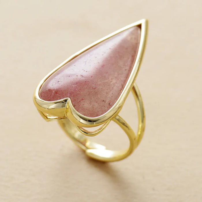 Gold ring with a heart-shaped rosy pink Strawberry Quartz gemstone on a beige background