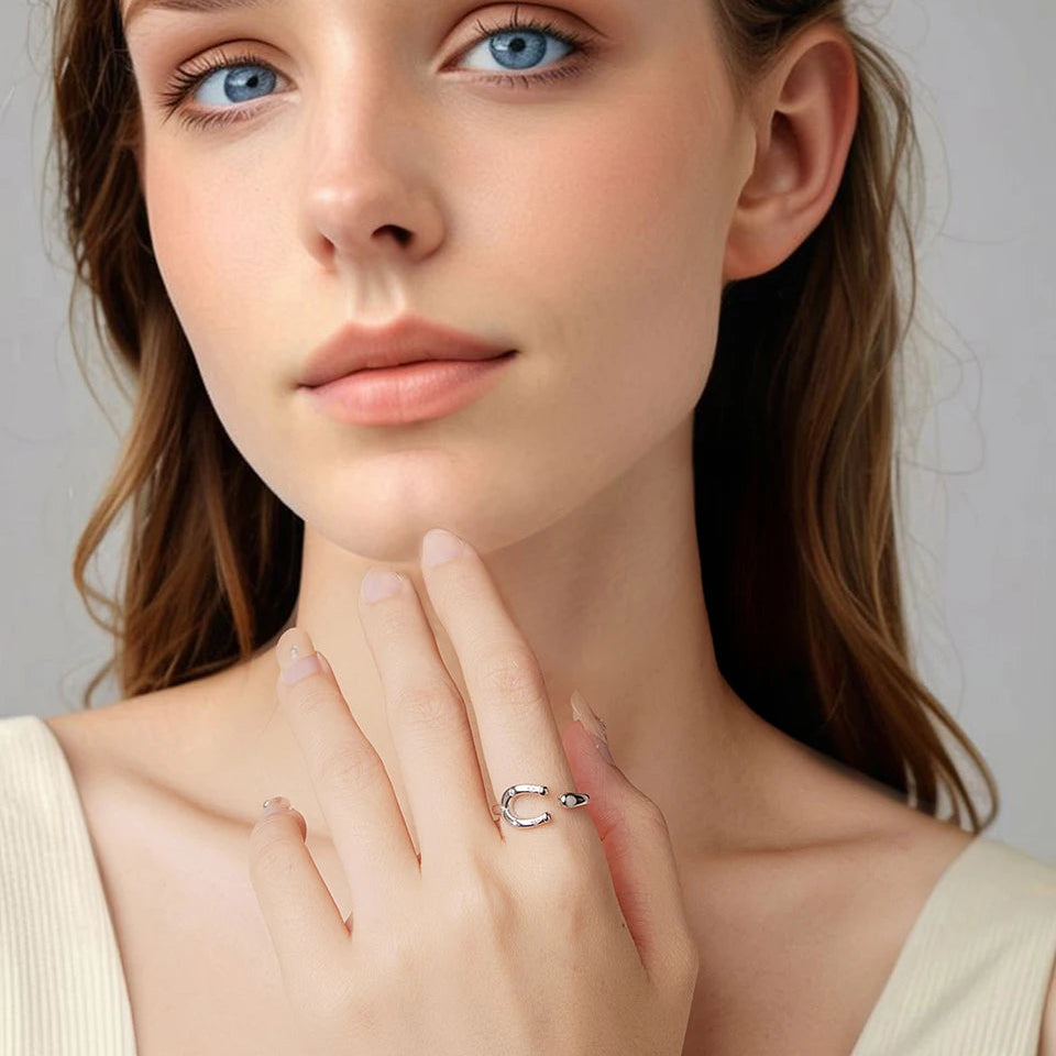 Close-up of a woman wearing a delicate horseshoe ring on her finger with a neutral background.